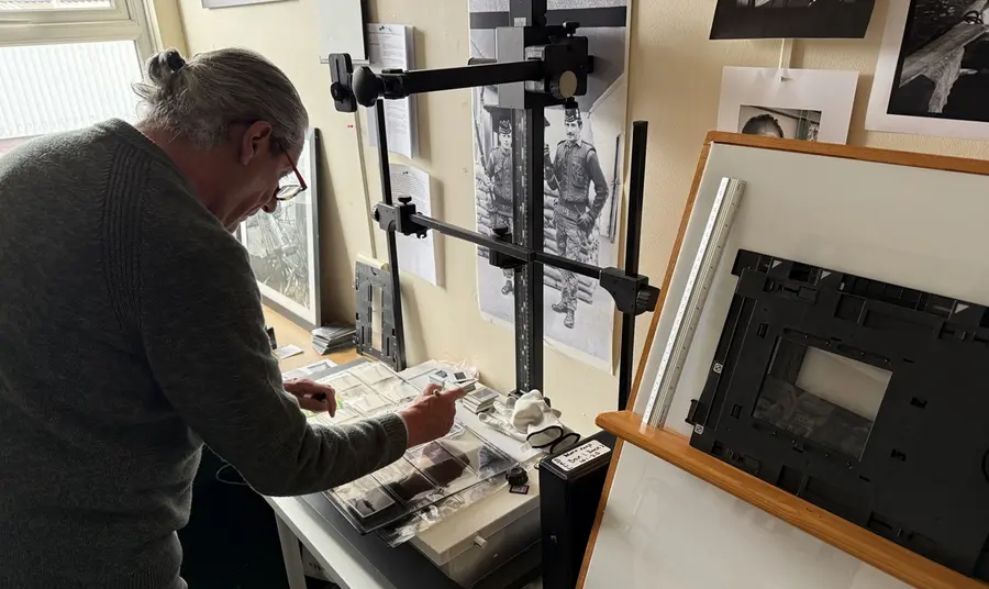 A project volunteer delicately scans negatives as part of the digitisation process, in a room with walls covered in photographs.