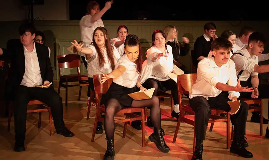 A group of young people sit on chairs and rehearse for a performance