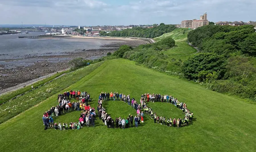 People gather to form the shape of the number 800 on a hill overlooking the mouth of the River Tyne, with the town of North Shields in the background.