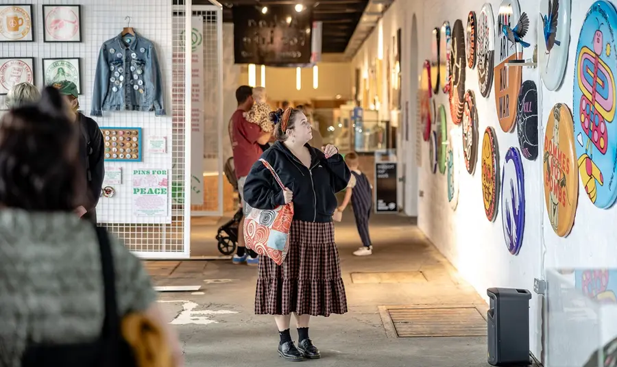 A young woman admires a wall display of oversized peace badges and pins on the wall of an exhibition space.