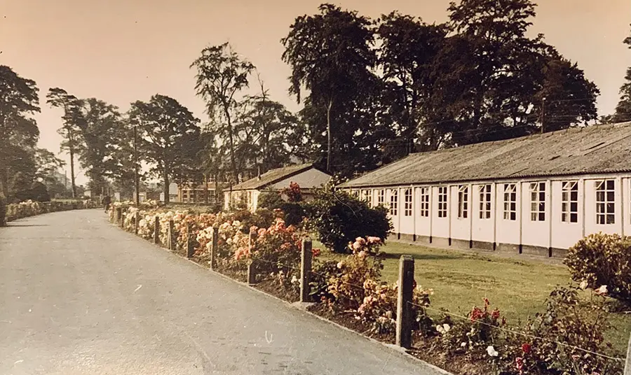 An old photograph of a barracks with flowerbeds in front