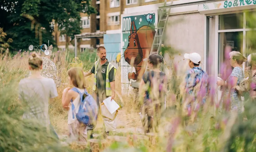 A guide wearing a high vis jacket shows a group of people around a lush meadow of long grass.
