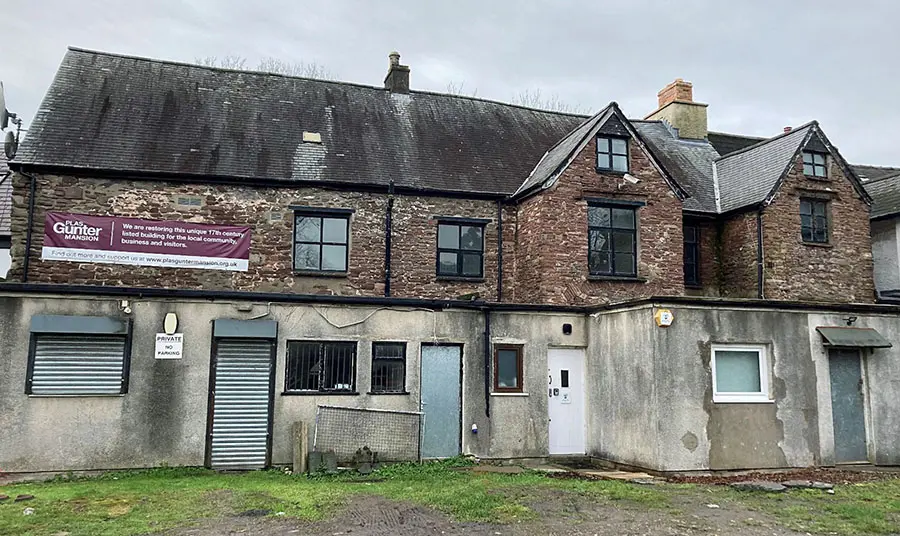 The exterior of a 17th-century building with modern additions in a state of disrepair