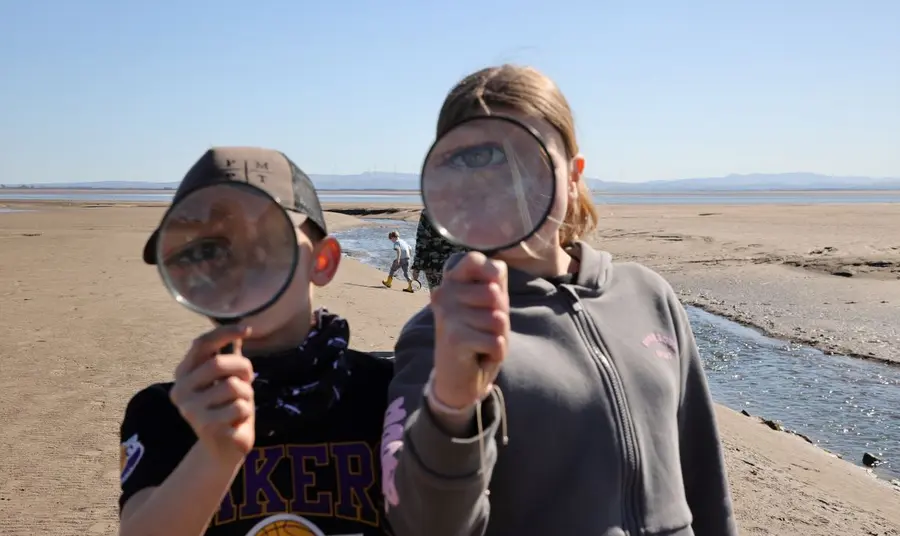 Looking at the camera, two children hold up magnifying glasses to their faces - obscuring their features but magnifying their eyes.