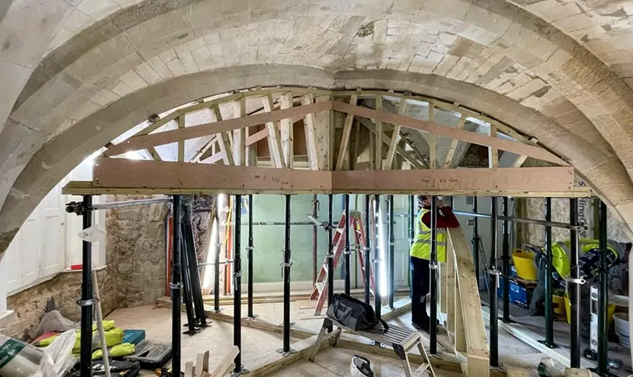 A stone cellar with building equipment and props supporting the ceiling.