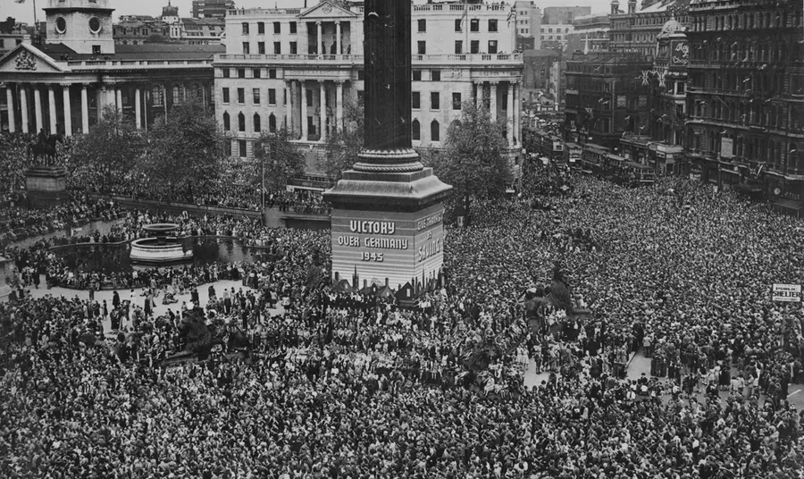 Public celebrations of VE Day in Trafalgar Square, May 1945. A black and white photograph showing an aerial view of Trafalgar Square on VE Day, with crowds of people coming together and filling the space.