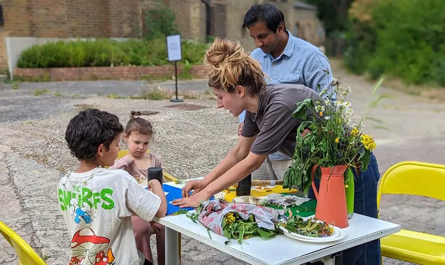 Two adults and two children do activities with flowers at a table in a courtyard