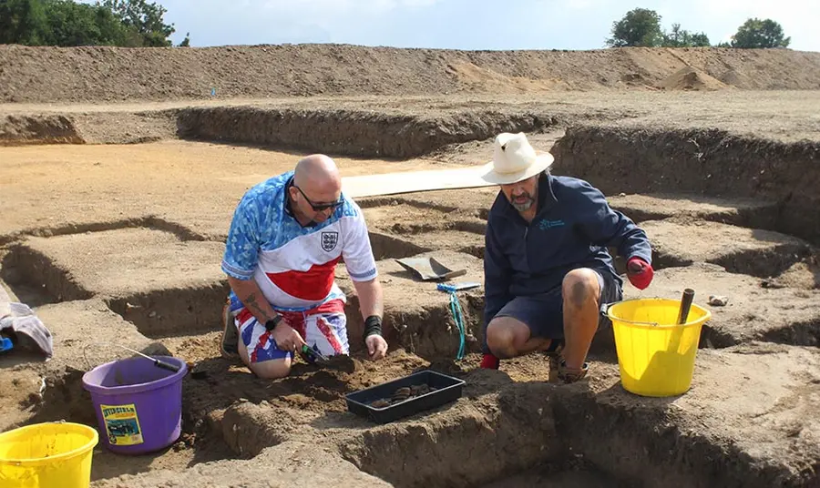 Two men digging in an archaeological excavation pit in summer