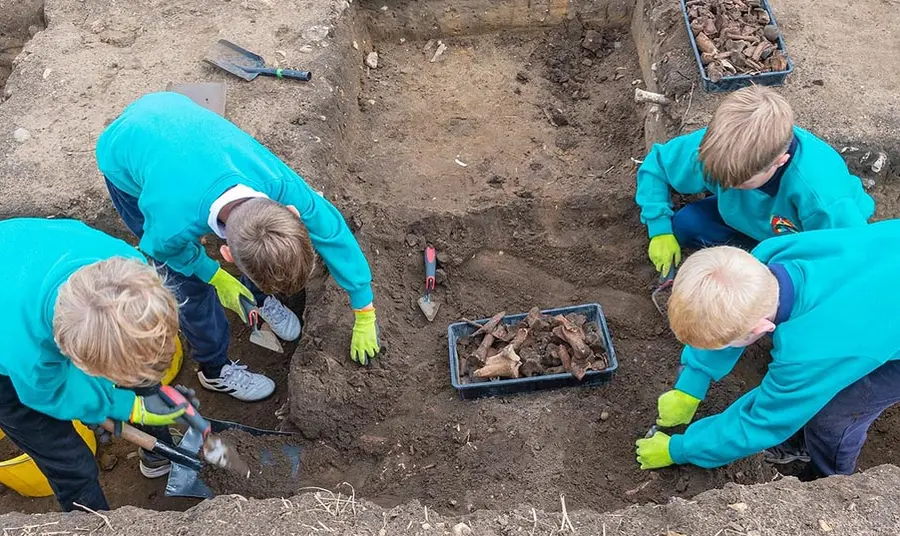 Four children digging with trowels in an archaeological pit