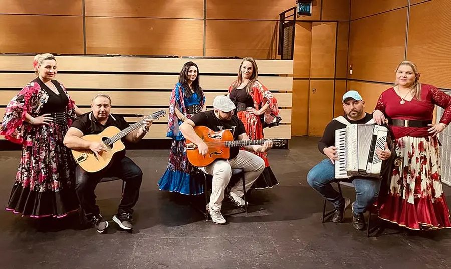 Three musicians with guitars and an accordion and four women dancers wearing traditional Eastern European dress.
