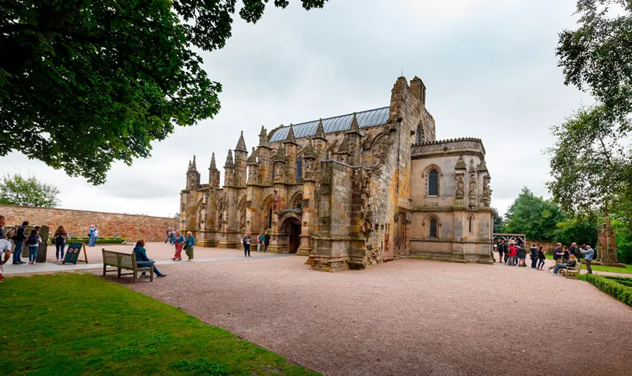 An ornate church, with a gravel path leading up to it, and grass on either side. There are people entering and exiting from the front and side of the church.