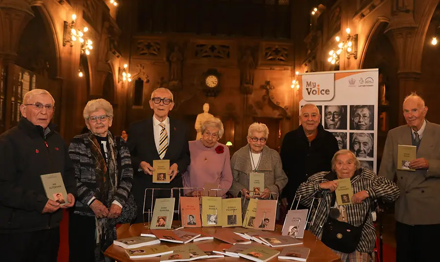 Holocaust survivors and refugees stand with their life story books in Sir John Rylands Library.