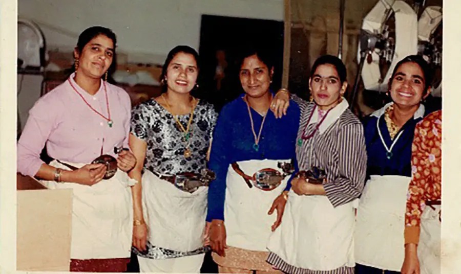 A group of people wearing aprons posing on a mill floor.