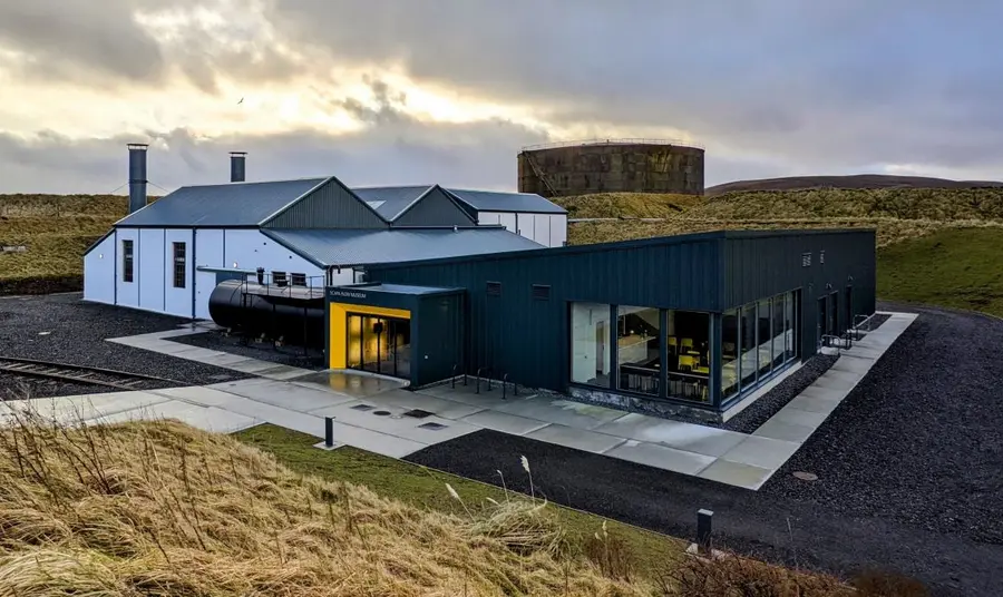 The Scapa Flow Museum, with an older structure of white warehouse spaces to the left, connected to a contemporary, single-storey expansion to the right, with a new entrance and café visible.