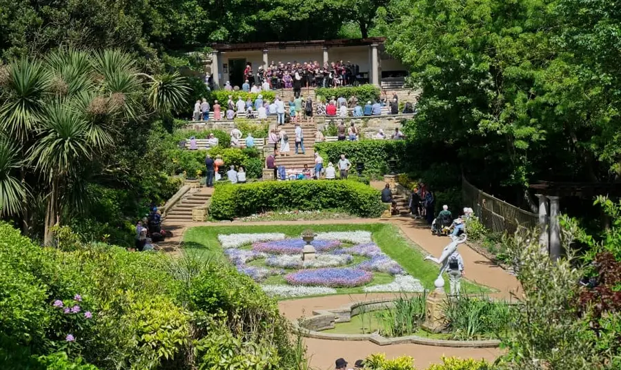 A large group of people standing on steps in a garden watching a performance.