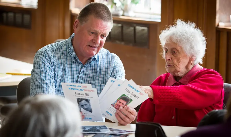 Community members at a Sporting Memories Club. A volunteer looks through memory cards of sportspeople with an older woman, during a Sporting Memories Club session.