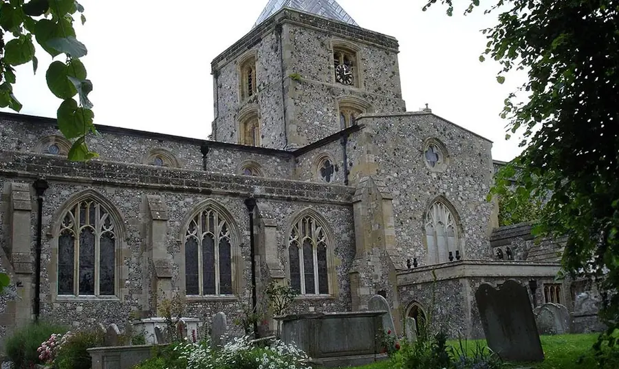 The exterior of St Nicholas Church in Arundel - a small parish church with a tower, surrounded by trees and a graveyard
