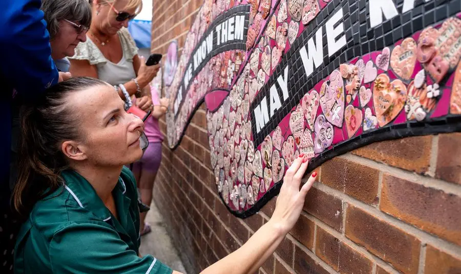 A person in a medical uniform looking at and touching the ceramic Strong Women mural
