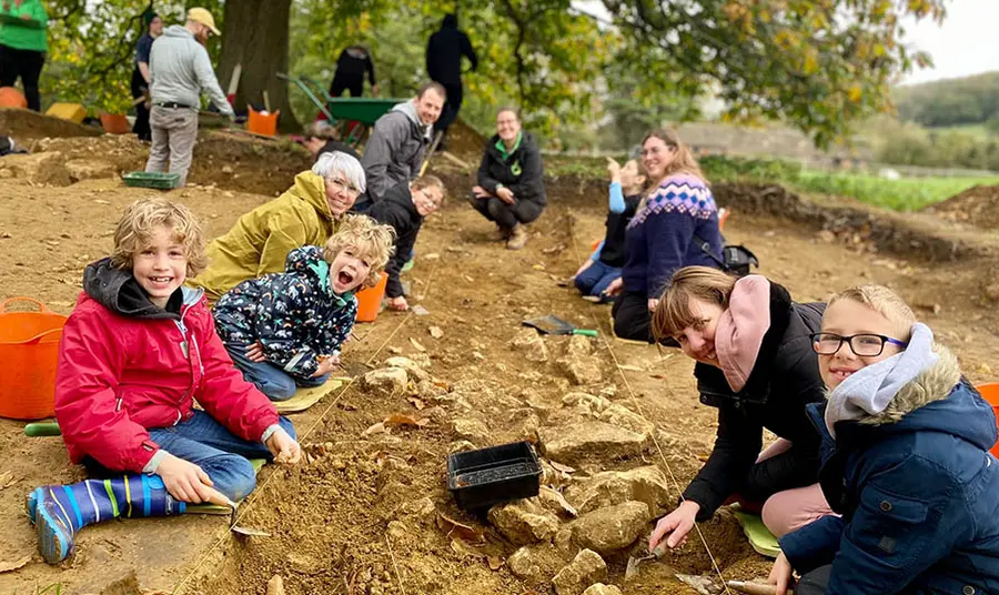 A group of people including adults and young people dig an archaeological trench