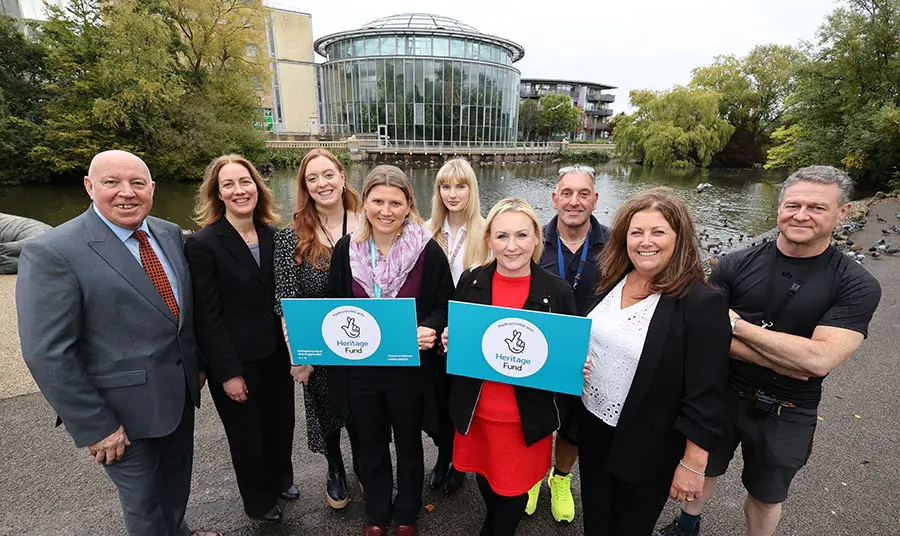 Grŵp o bobl yn dal placiau cydnabyddiaeth y Gronfa Treftadaeth o flaen Sunderland Winter Gardens, adeilad gwydr crwn modern