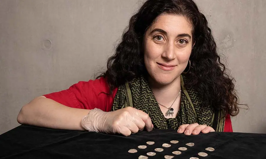 Amal Khreisheh leans over a table displaying rows of coins from the Chew Valley Hoard