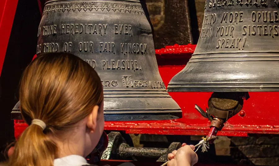 taylors_hero_1.jpg A visiting schoolgirl rings a cast iron bell on a bracket.