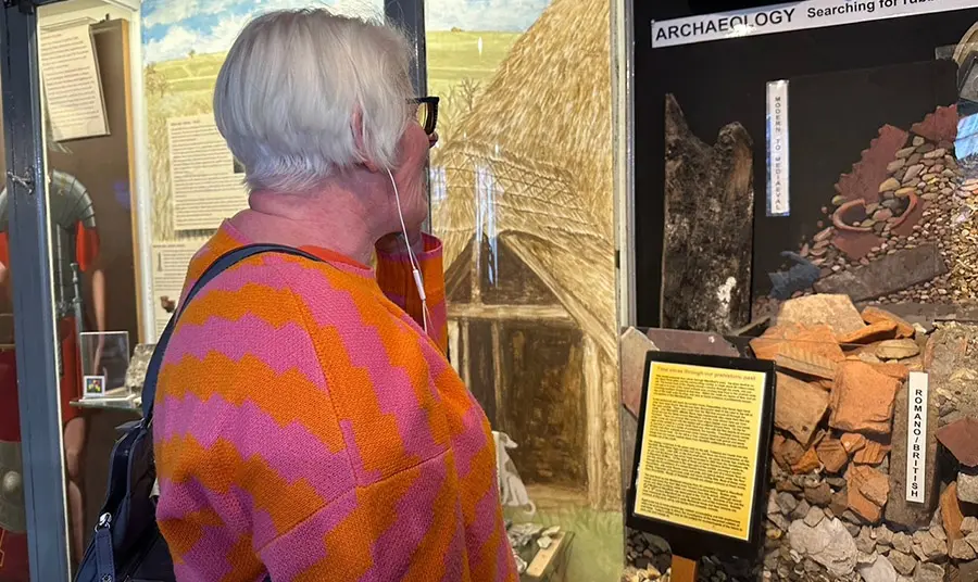 A person listening to audio through earphones in front of a display about archaeology showing different layers of artefacts