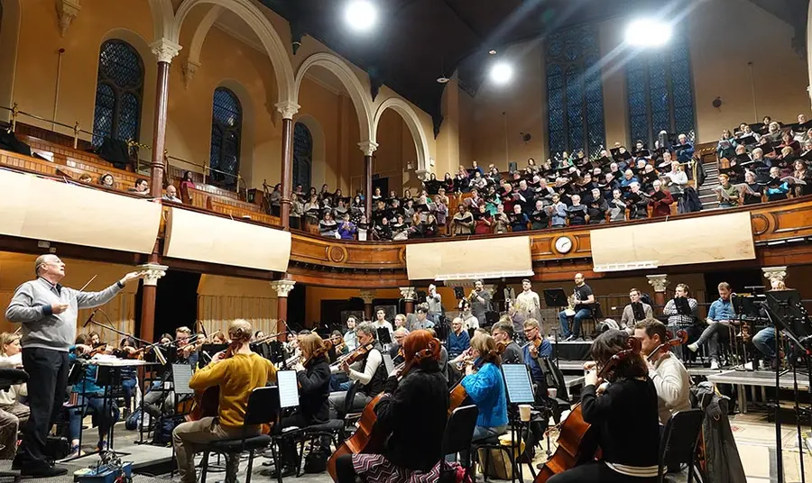a symphony orchestra rehearses inside a large church with a choir singing from the church's balcony