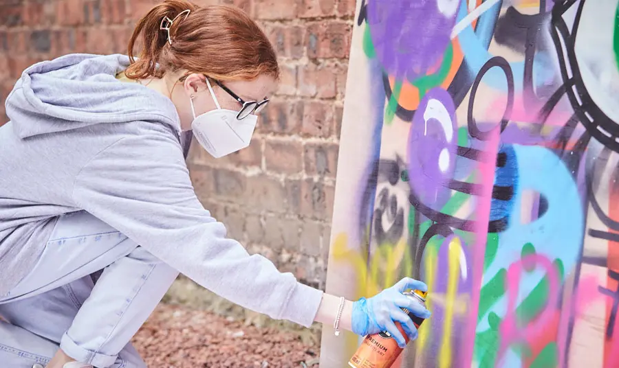 A young person creates a placard with spray paints