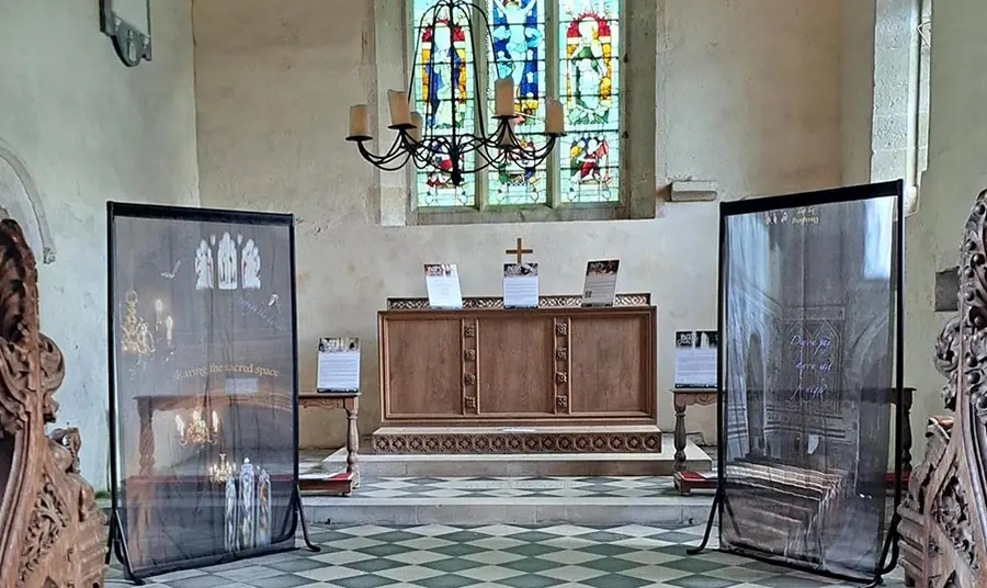 An interior shot of a small church. On either side of the altar are two panels with artwork featuring bats.