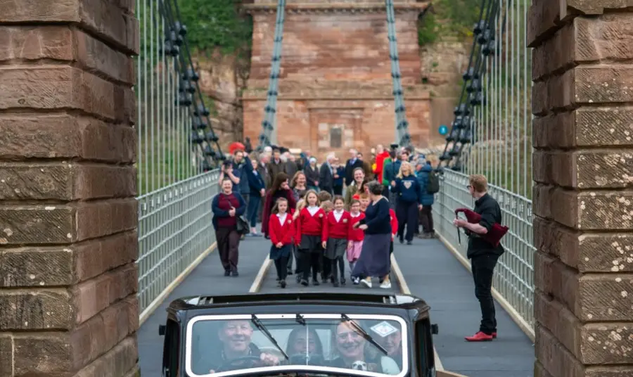 A vintage car and school children cross the Union Chain Bridge as it reopens to traffic.