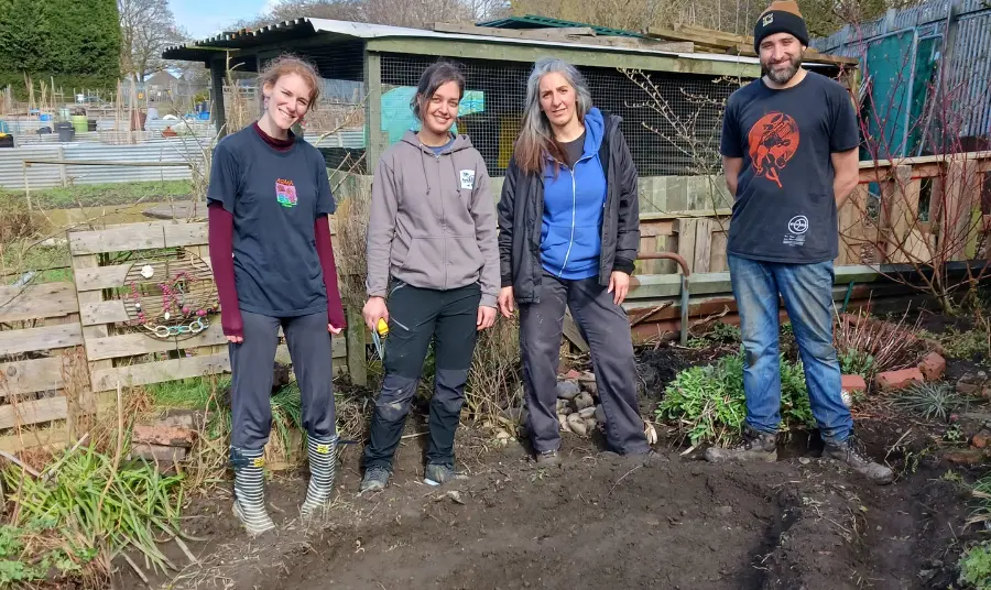 Photograph of four people standing in front of a dig.
