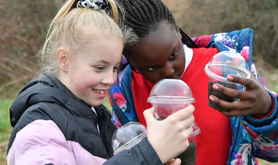 Two girls holding takeaway cups filled with soil