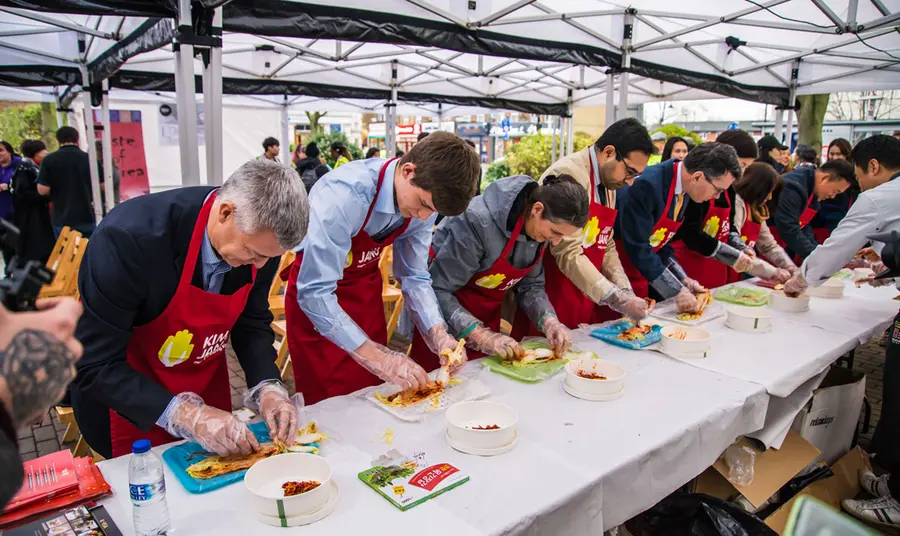 A group of people lined up behind a long table being taught how to make kimchi