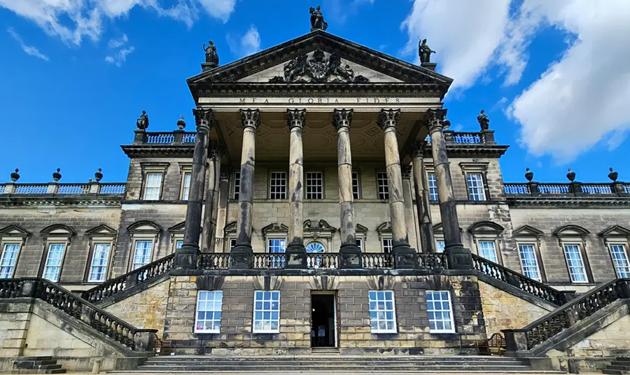 The facade of a stately home with a bright blue sky behind it