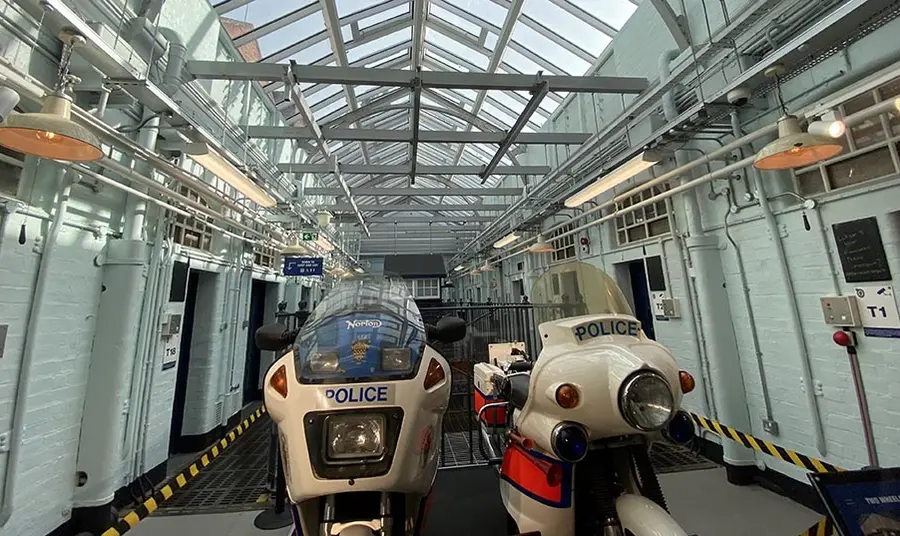 A photo of the inside of the police museum, in a Victorian jail building. Two police motorcycles are displayed on a landing, surrounded by cells, with a glass ceiling above.