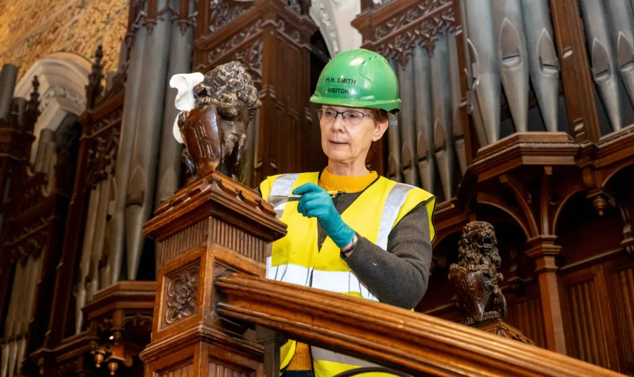 A volunteer using a paint brush to clean a wooden banister 