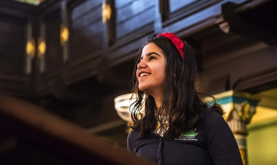 A young child in a school uniform looking up and smiling inside a synagogue 