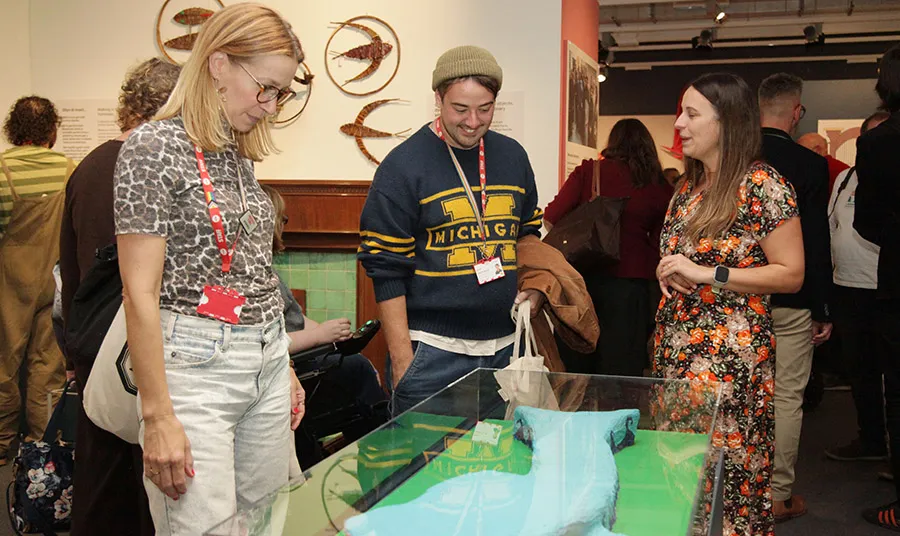 Three people look at a museum display containing a hand-crafted model of a whale
