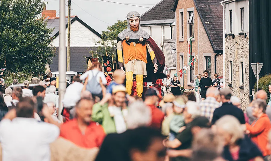 A crowd of people at a procession featuring a giant puppet of Lord Rhys, in Maenclochog.