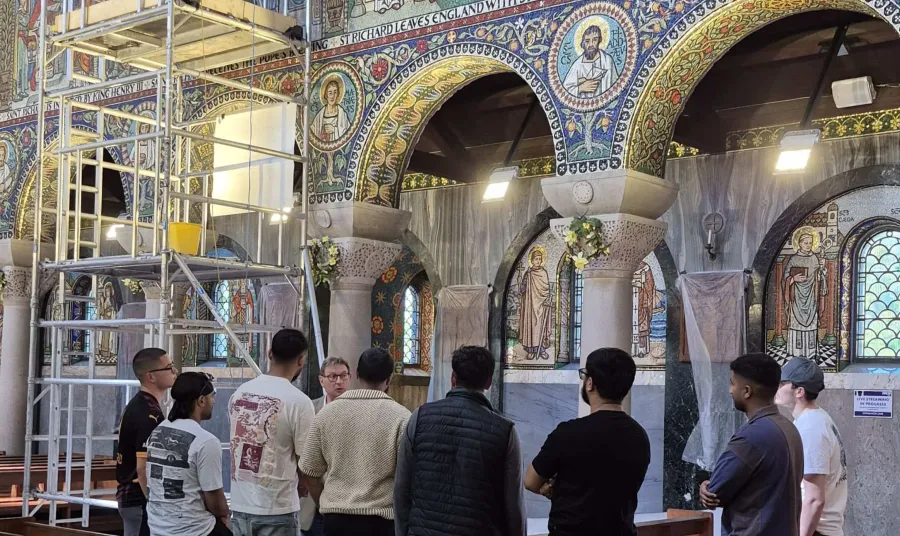 a group are given a tour of a church with mosaics under repair near a scaffolding tower