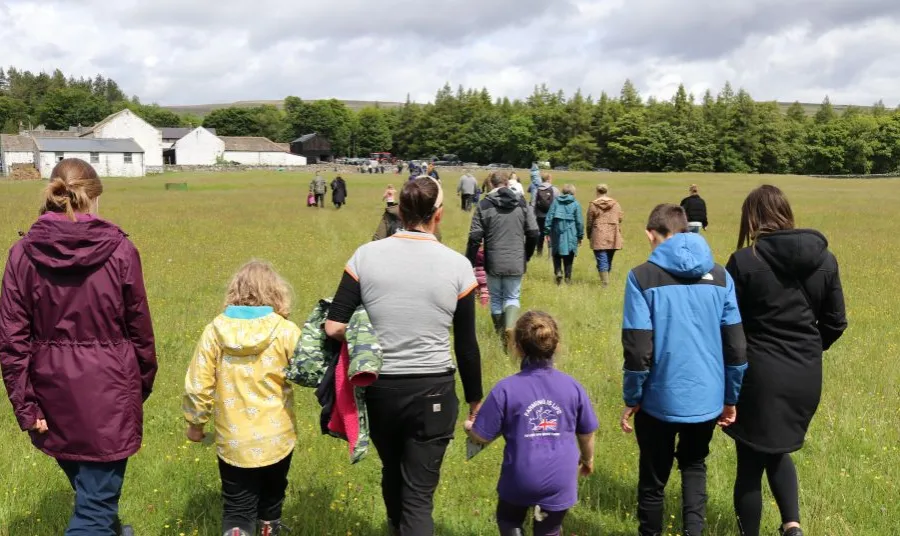 adults and children walk in a grassy field