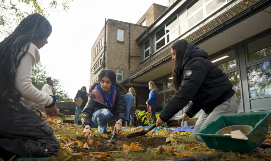 three young women dig a plot of ground marked with string with trowels