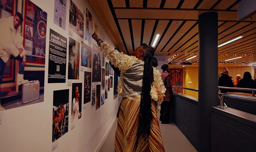 A person pointing at a gallery wall covered in pictures of dancehall artists