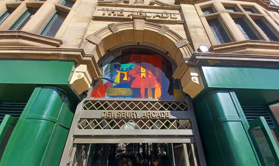The entrance to Dewsbury Arcade, with original stonework as well as newly painted shopfronts and a colourful glass panel above the door