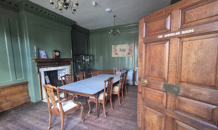 A door opens onto a historic wood panelled room painted in green with a dining table in the middle and a fireplace at the back