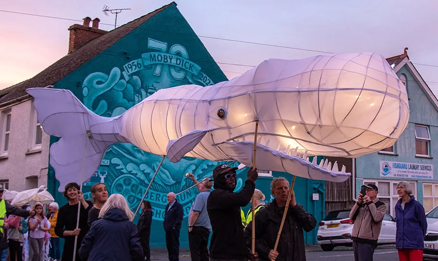 A large whale-shaped lantern being paraded in front of a mural of Moby Dick