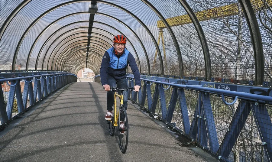A man cycling on a bridge with the Harland and Wolff cranes visible in the background