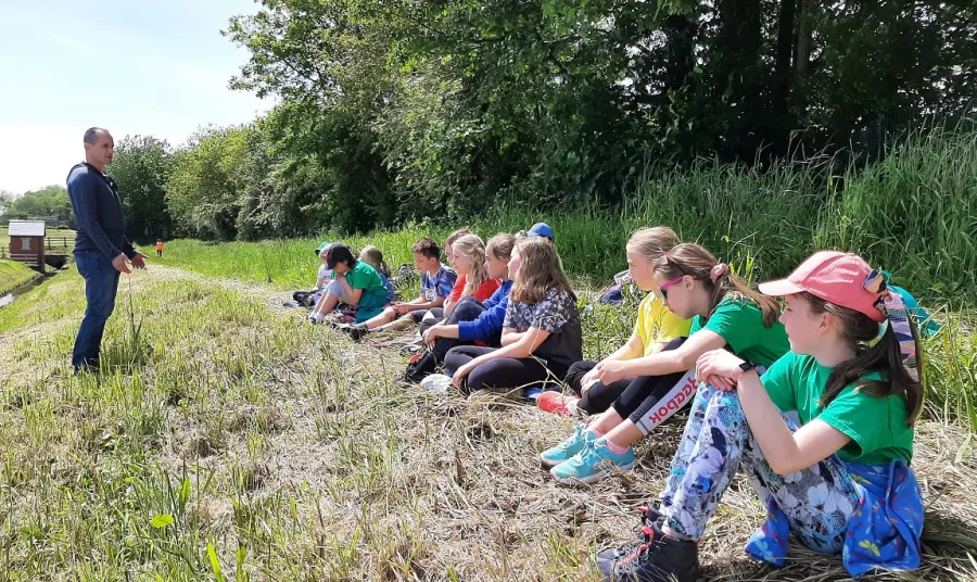 Grŵp o blant yn eistedd i lawr o flaen rhes neu goed, yn gwrando ar rywun yn rhoi sgwrs
