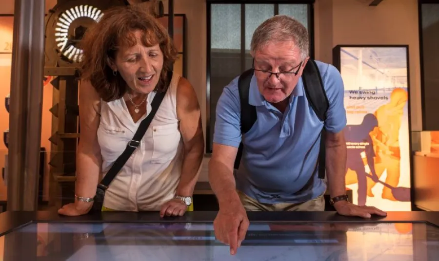 An older man and women using a digital interactive table exhibit at a museum
